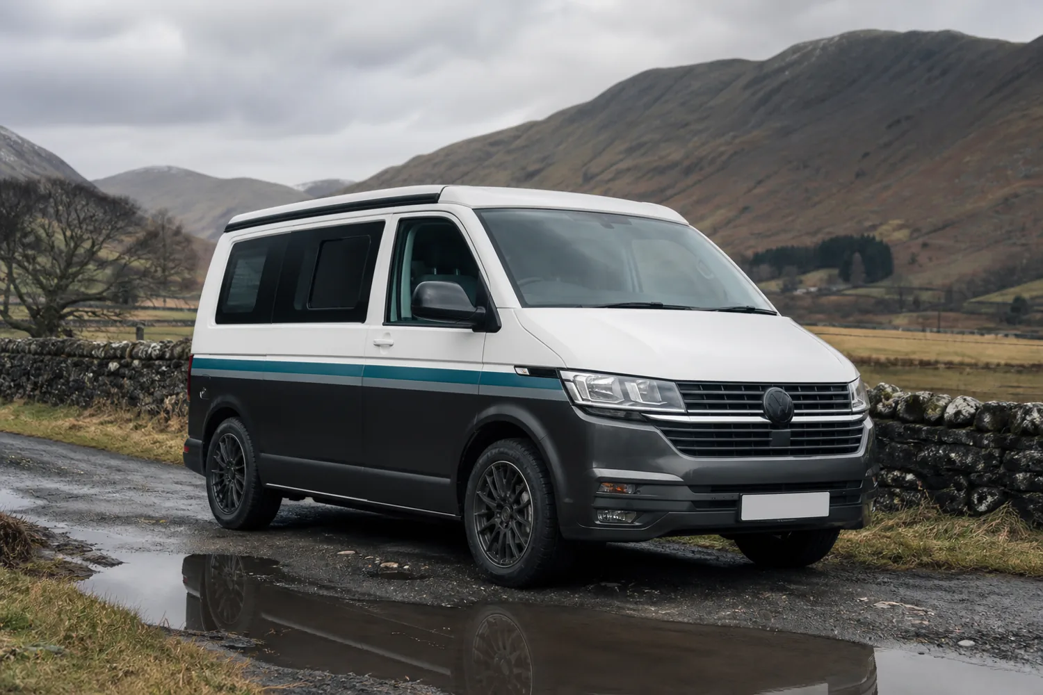 VW Transporter camper with two-tone wrap and side stripe, parked on a wet Lake District lane