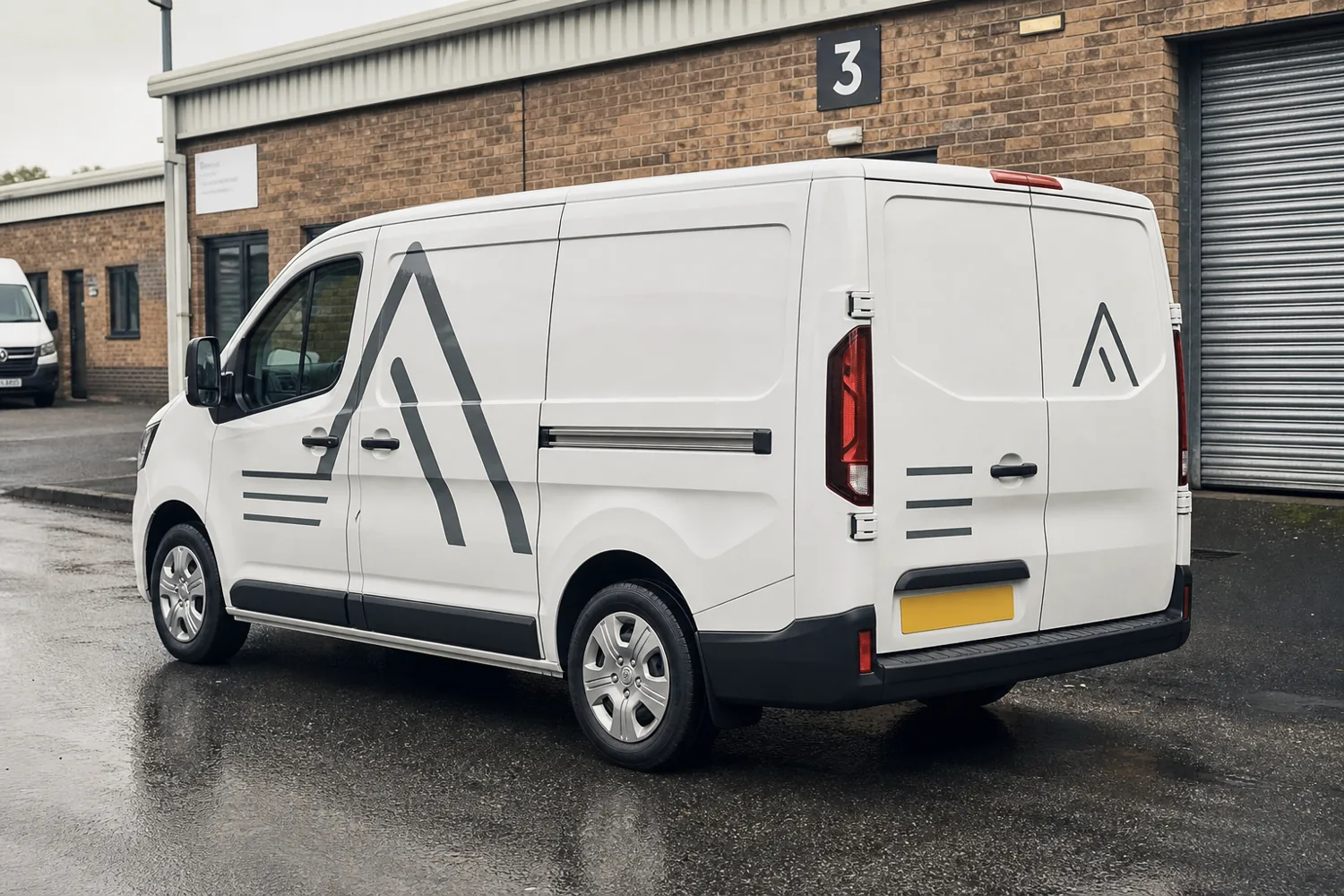 Trades van with clean vinyl side lettering on wet tarmac outside workshop units in Kendal